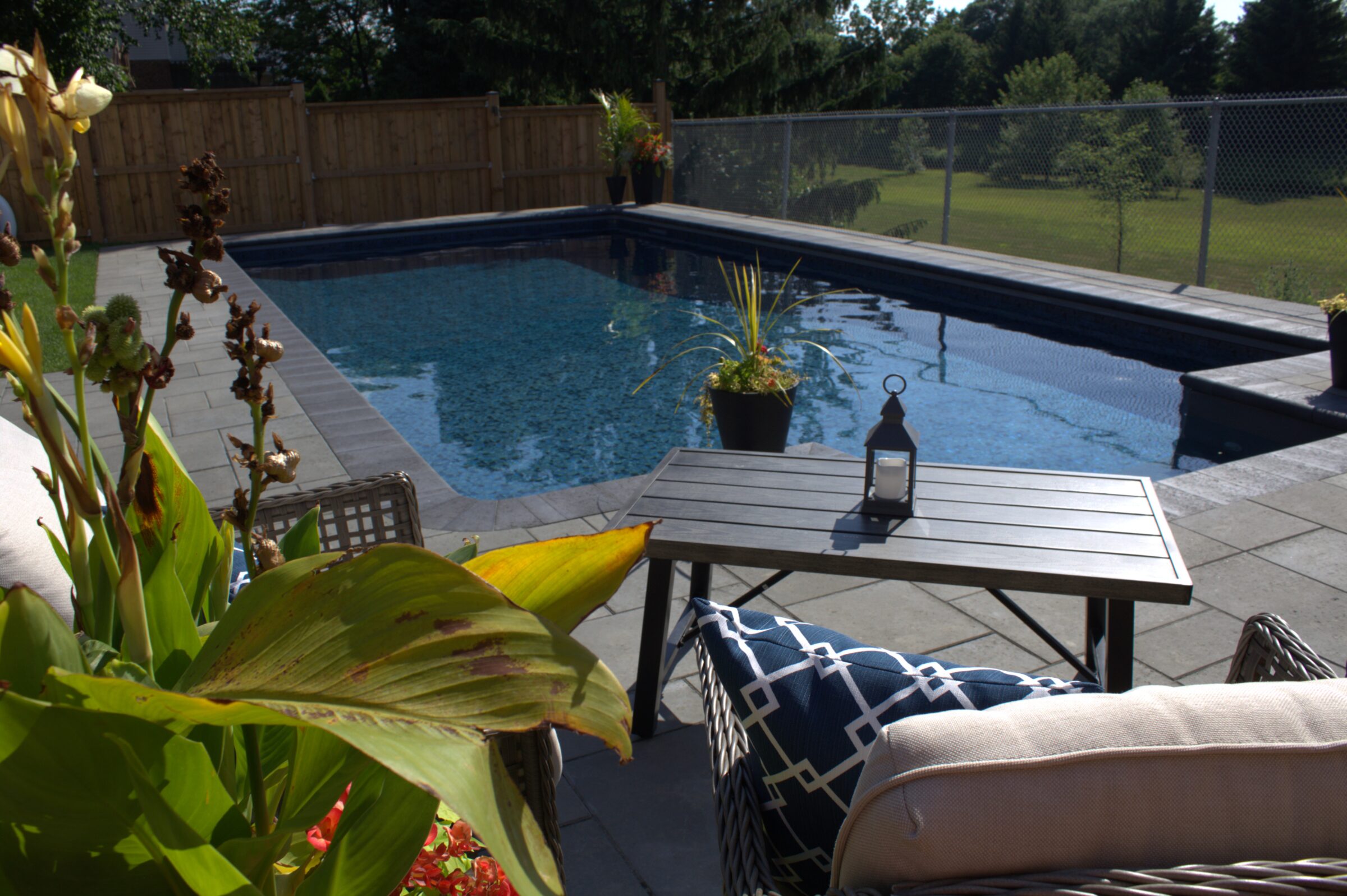 A tranquil backyard with a pool, lounge chairs, and lush plants. Wooden fence and lantern create a peaceful outdoor atmosphere.