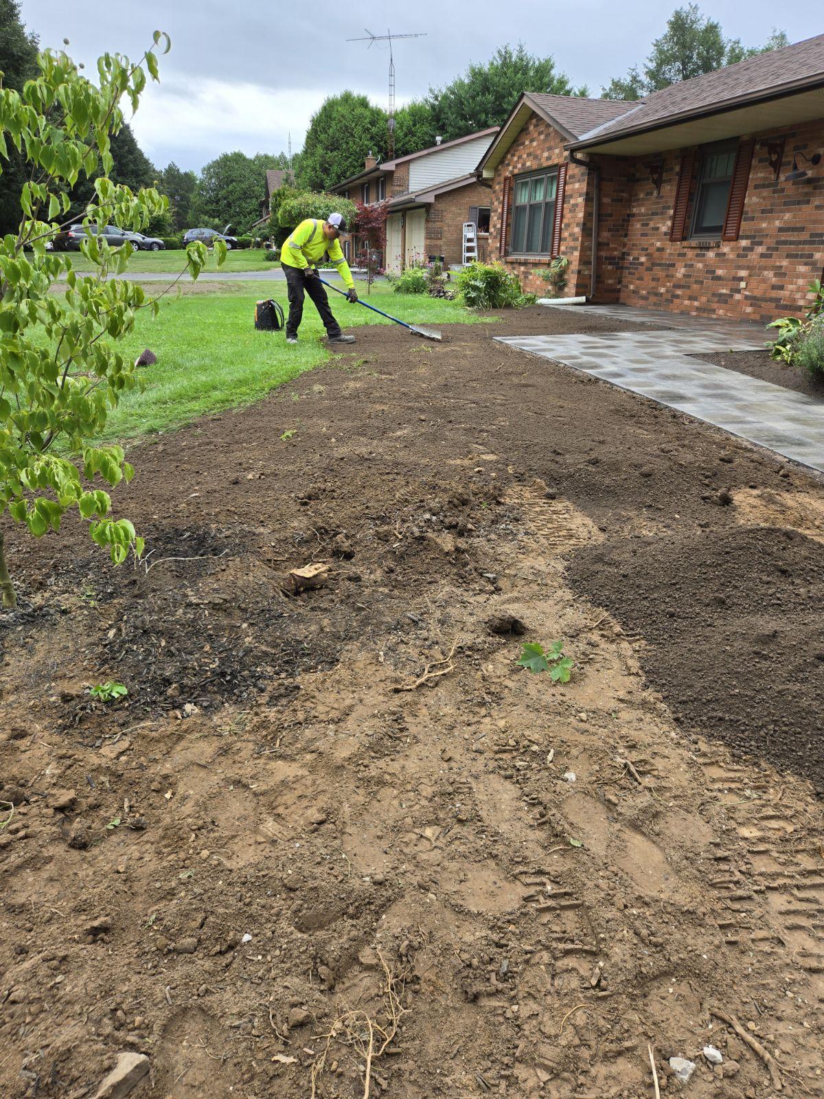 Worker grading soil beside front walkway